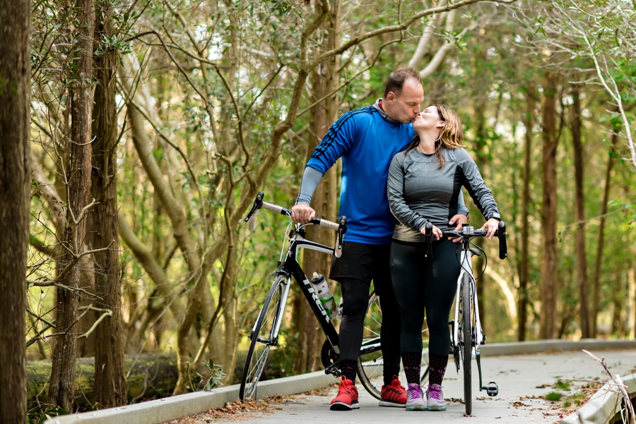 An athletic couple kiss while holding their bikes during their cape may engagement session.
